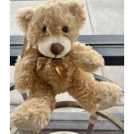 A tan teddy bear with a ribbon sits on a chair.