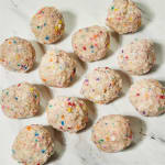 Nine sprinkle-covered dessert balls on a white surface