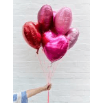 Hand holding a bunch of pink and red heart-shaped balloons