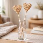 Clear glass vase with two woven rattan heart picks on sticks on a table