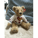 Teddy bear wearing a white sweater with heart patterns