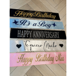 Five decorative birthday and anniversary ribbon banners laid on a tiled floor