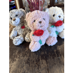 Three plush teddy bears with ribbon roses sit on a table.