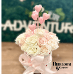 Round box of pale pink and white roses topped with pink heart picks