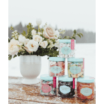 White and blush flower arrangement in a white vase beside stacked jars of colorful candy on a snowy table.