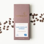 Dark chocolate espresso bar in mauve wrapper with scattered coffee beans on white background