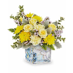 Compact arrangement of yellow and cream flowers in a square glass vase with a dove design