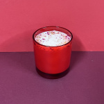 Red glass candle with a white wax top and flower petals