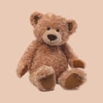 Plush teddy bear sitting against a plain peach background