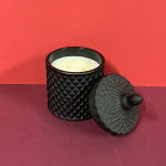 Black textured candle jar with lid on a red background