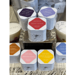 Assorted scented candles in white metal tins stacked on a wooden display