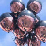 Cluster of metallic black and rose-gold balloons against a blue sky