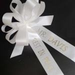 White ribbon bow with printed memorial text on a black surface