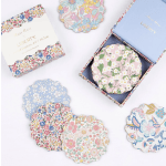 Floral-patterned scalloped coasters and a matching box on a white surface