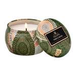 Patterned green candle in a round tin with a lit wick