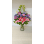 Mixed bouquet of pink lilies, roses, and purple flowers in a clear glass vase