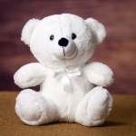 White teddy bear with a satin ribbon sitting on a brown surface