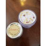 A lavender candle jar with dried flower petals and a metal lid labeled "Goddess."