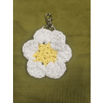 Crocheted white and yellow flower keychain on a green fabric background