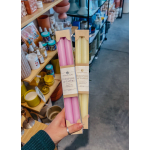 Hand holding two boxed sets of pink and pale yellow taper candles in a gift shop.