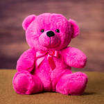 Bright pink teddy bear with a satin bow sitting on a surface