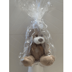 Plush teddy bear wrapped in clear cellophane with white ribbon curls