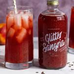 Glass of red sangria beside a labeled bottle with a straw