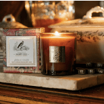 Lit amber candle in a glass jar beside a decorative candle box
