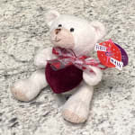 White teddy bear holding a red heart with a gift tag