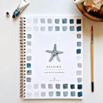 Watercolor workbook with a starfish cover and paintbrush beside it