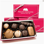 Box of assorted chocolates with pink gift boxes behind it
