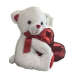 White teddy bear holding red heart pillows with a red ribbon
