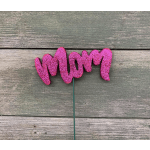 Pink glitter "Mom" pick on a green stem against wood