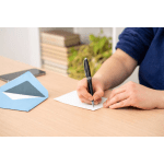 Person writing a note beside an open envelope on a desk