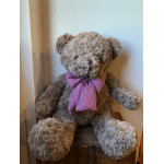 A plush teddy bear with a red gingham bow sits on a wooden crate.
