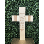 Wooden memorial cross with engraved text against a green foliage wall