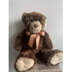 Brown teddy bear with a satin bow sitting against a plain wall