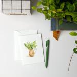 Greeting card with a watercolor potted plant illustration beside an envelope and pen