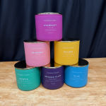 Five colorful scented candles stacked in a pyramid on a wooden surface