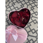 Heart-shaped box filled with dark red rose petals and a pink ribbon lid
