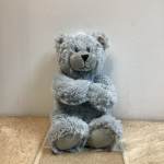 Gray plush teddy bear sitting upright with paws crossed