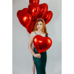 Woman holding red heart-shaped balloons against a plain background
