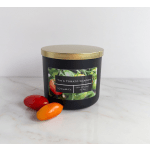 Black candle tin with gold lid and tomato-themed label, beside two small tomatoes