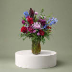 Mixed bouquet of red, purple, and blue flowers in a glass vase