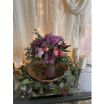 Purple and pink floral arrangement in a mauve vase with candles nearby