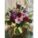 Mixed bouquet of roses, gerbera daisies, lilies, and purple daisies in a glass vase
