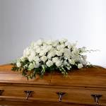 White rose casket spray arranged on a polished wooden coffin