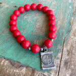 Red beaded bracelet with a silver charm on a wooden surface
