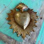 Gold heart-shaped religious wall ornament on a turquoise wooden surface