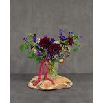 Purple and burgundy flowers in a clear glass vase on a wood slab